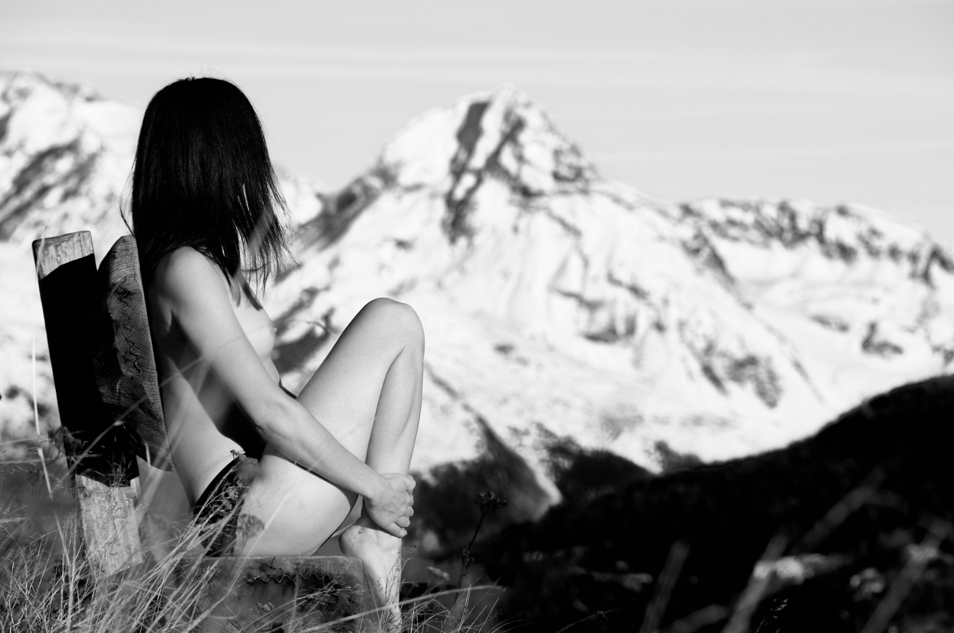 Femme nue assise sur un banc, sommet enneigé en arrière plan